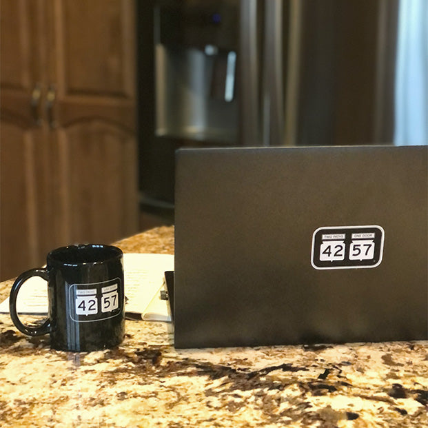 42-57 ceramic mug next to a laptop with a 42-57 sticker