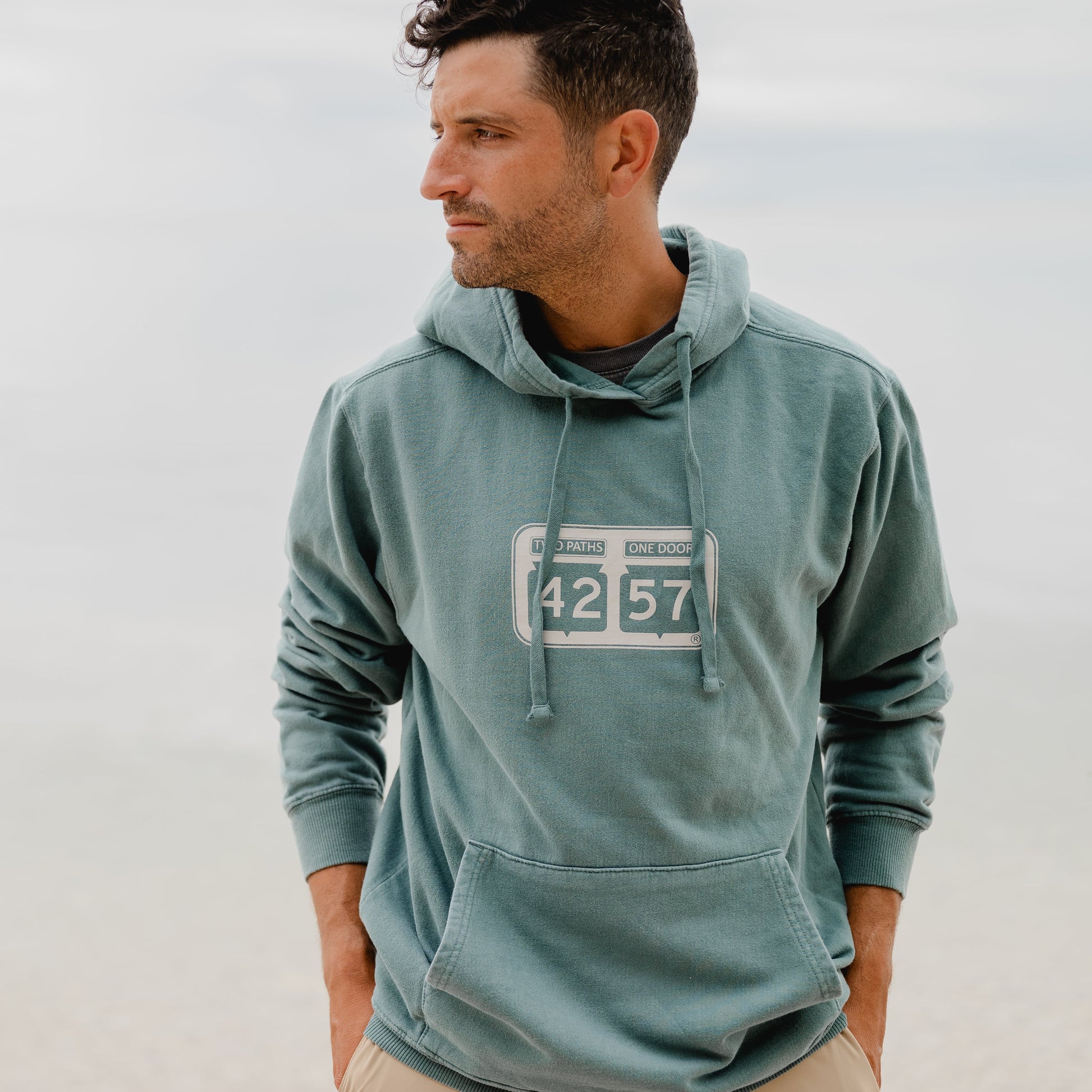 Model wearing 42-57 Unisex Shoreline Hoodie in green during a Door County summer evening
