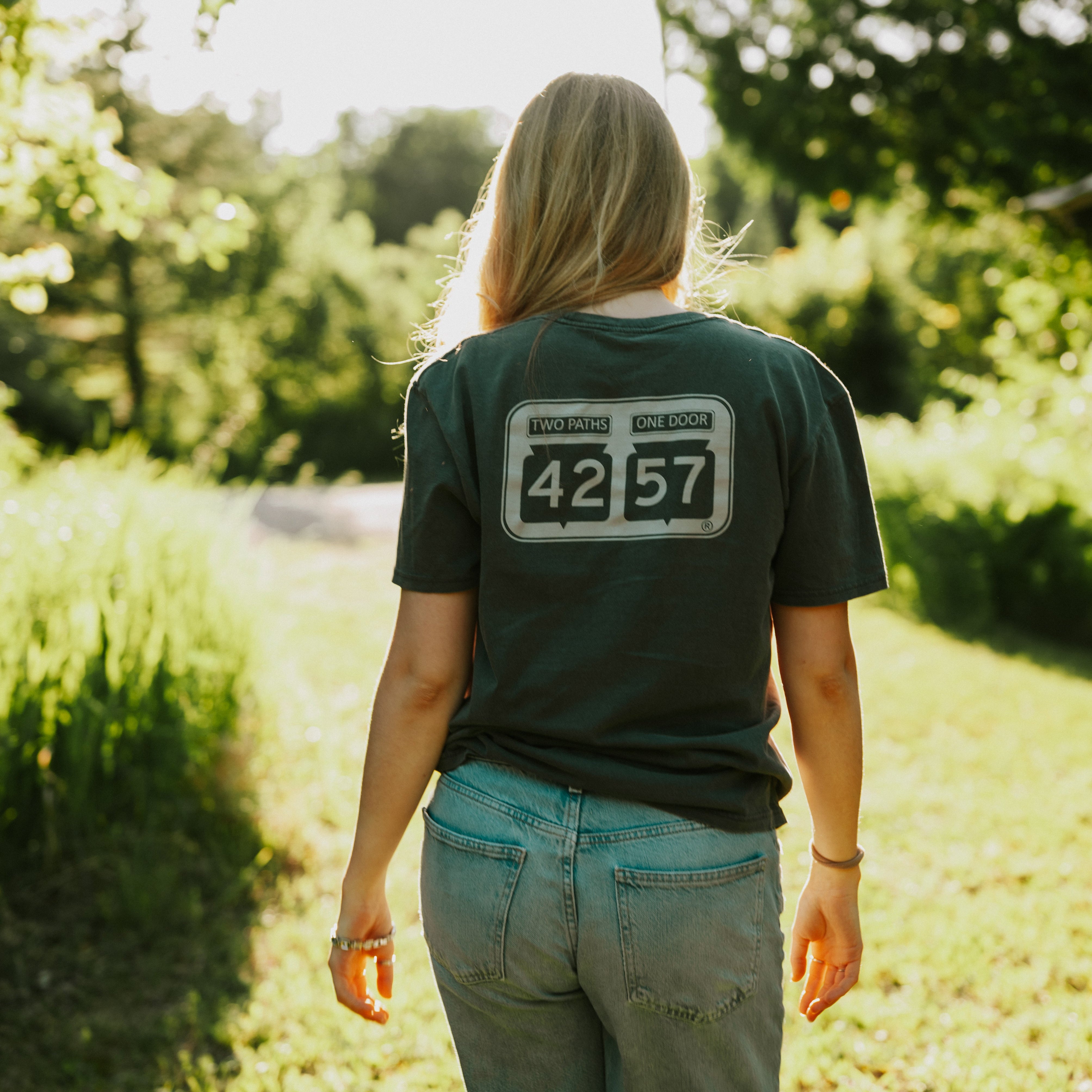 Model wearing 42-57 Unisex Shoreline Tee in heather gray in a Door County shoreline setting